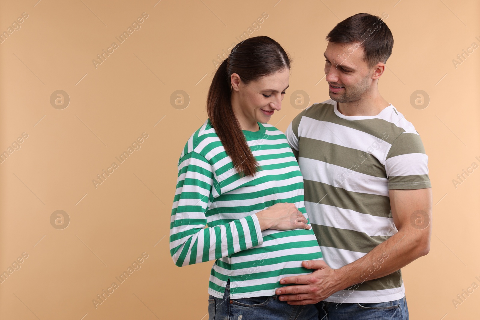 Photo of Pregnant woman and her husband on beige background. Space for text