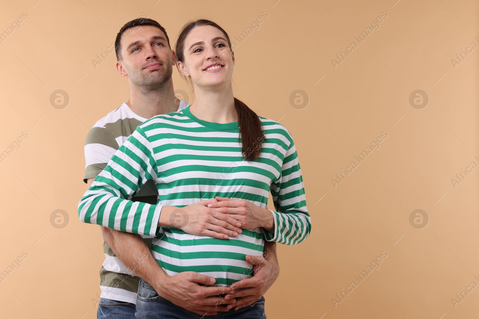 Photo of Pregnant woman and her husband on beige background. Space for text