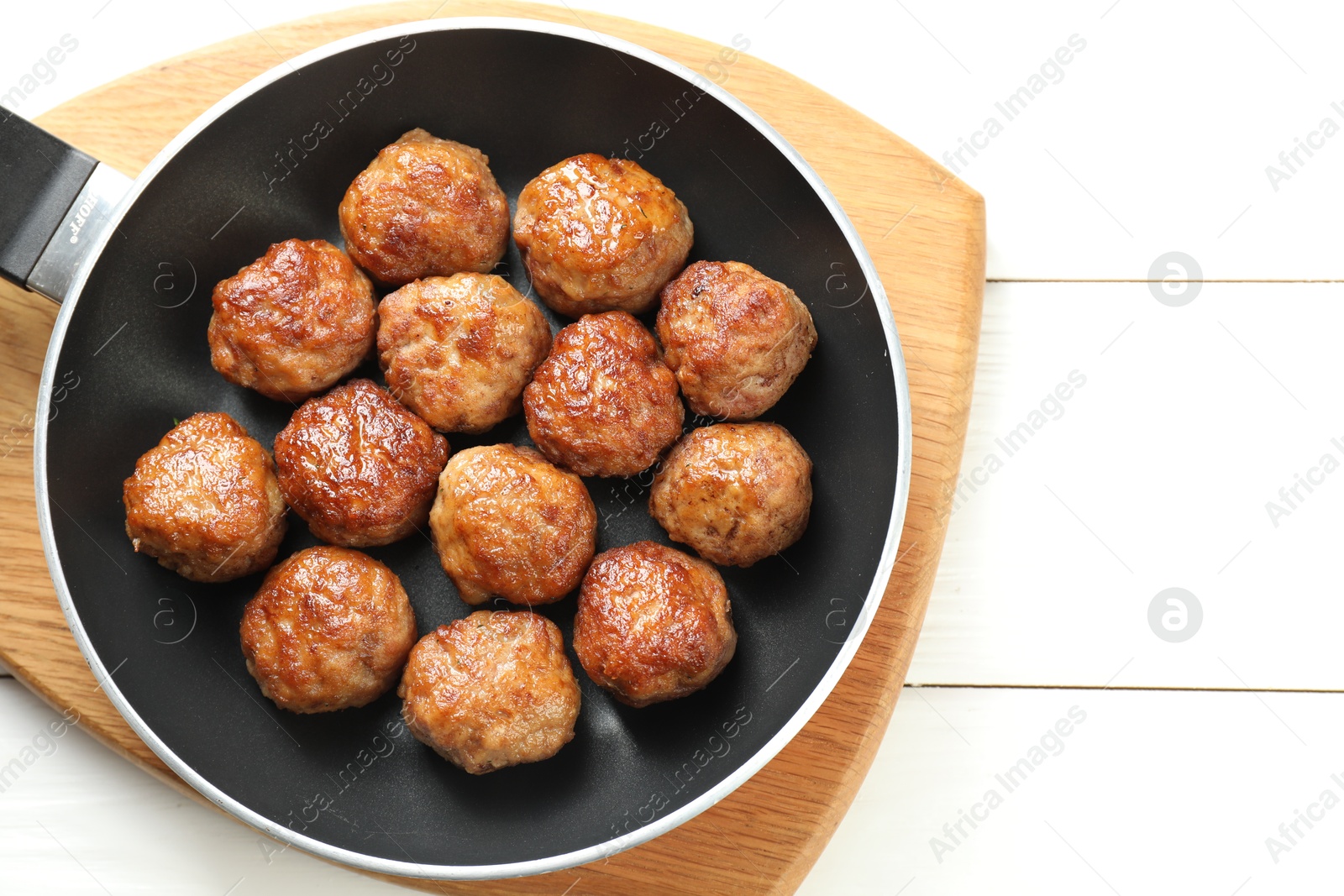 Photo of Tasty meatballs in frying pan on white wooden table, top view. Space for text