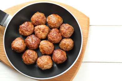 Photo of Tasty meatballs in frying pan on white wooden table, top view. Space for text