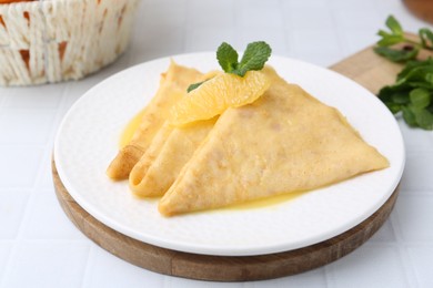 Photo of Tasty crepes Suzette on white tiled table, closeup