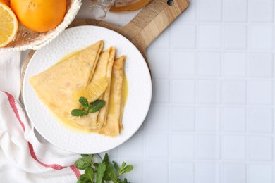 Photo of Tasty crepes Suzette and products on white tiled table, flat lay. Space for text