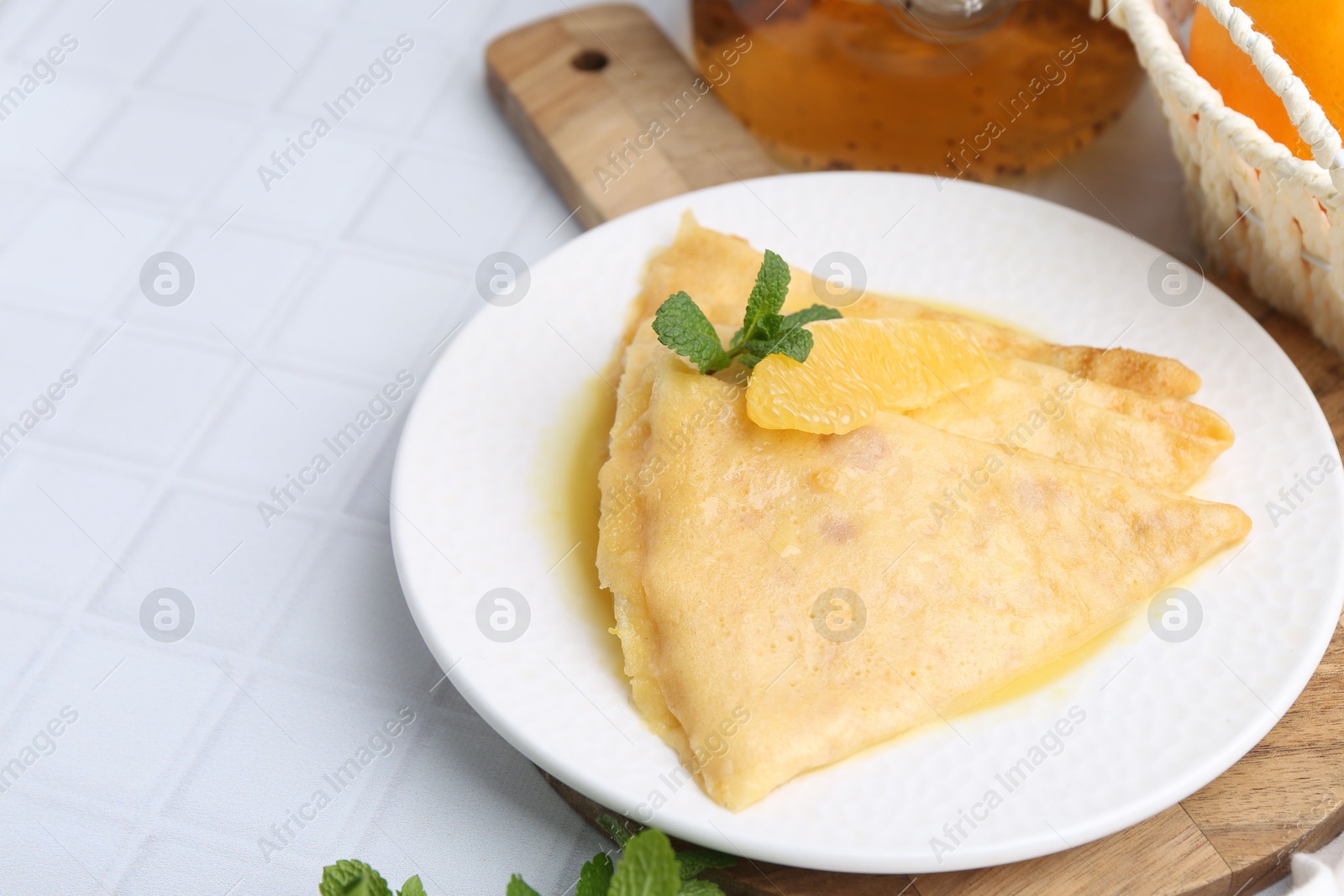 Photo of Tasty crepes Suzette on white tiled table, closeup. Space for text