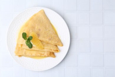 Photo of Tasty crepes Suzette on white tiled table, top view. Space for text