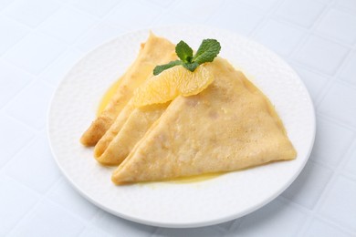 Photo of Tasty crepes Suzette on white tiled table, closeup