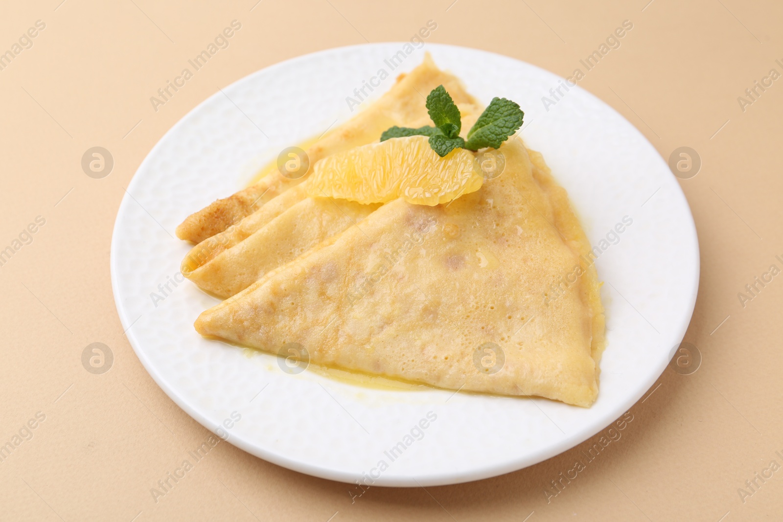 Photo of Plate with tasty crepes Suzette on beige table, closeup