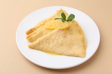 Photo of Plate with tasty crepes Suzette on beige table, closeup