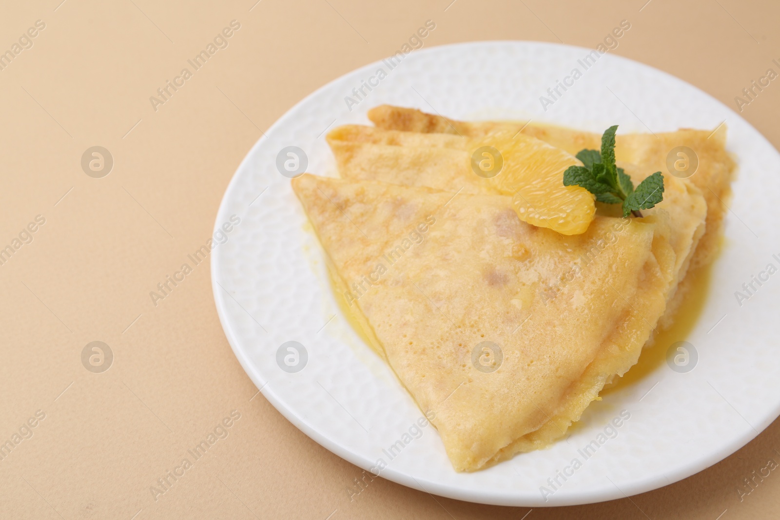 Photo of Plate with tasty crepes Suzette on beige table, closeup. Space for text