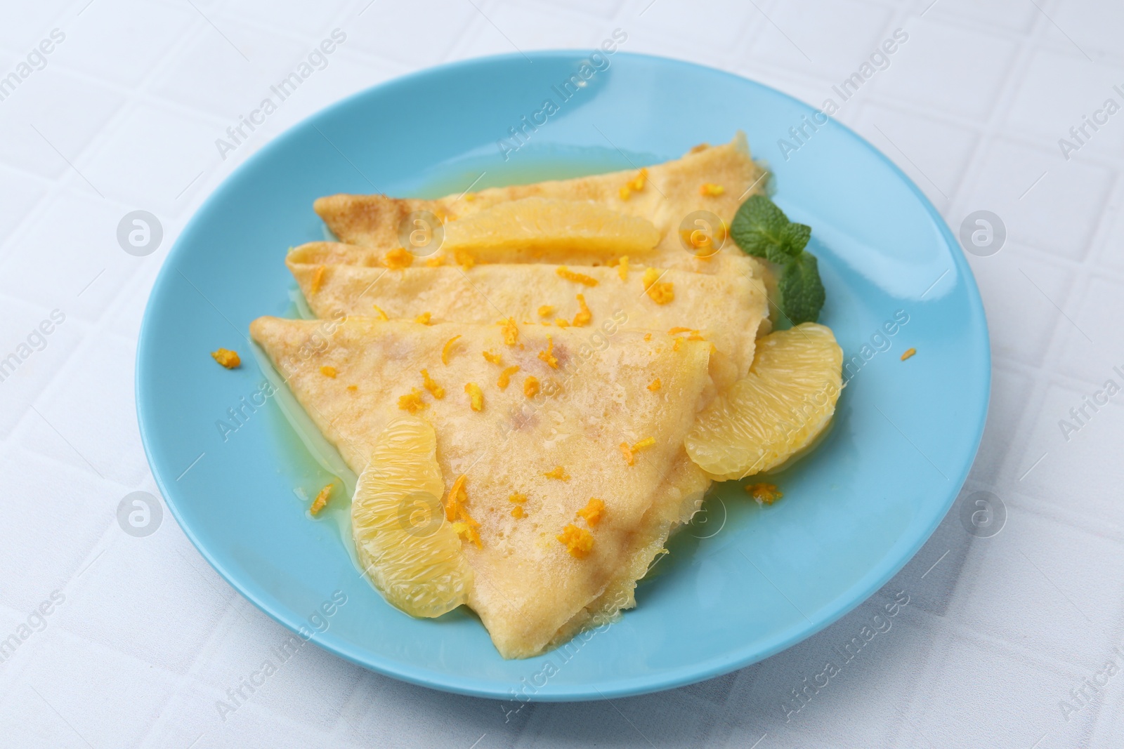 Photo of Tasty crepes Suzette on white tiled table, closeup