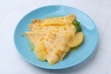 Photo of Tasty crepes Suzette on white tiled table, closeup