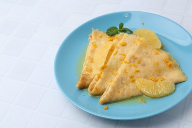 Photo of Tasty crepes Suzette on white tiled table, closeup. Space for text