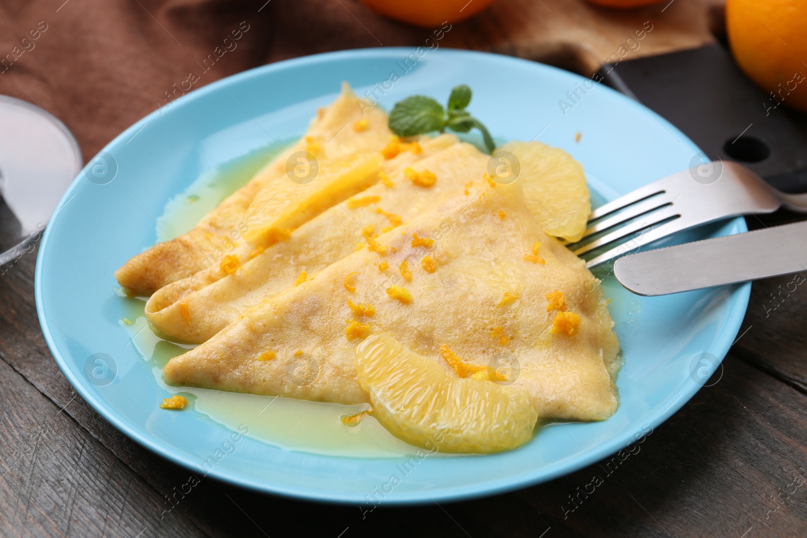 Photo of Plate with tasty crepes Suzette on wooden table, closeup