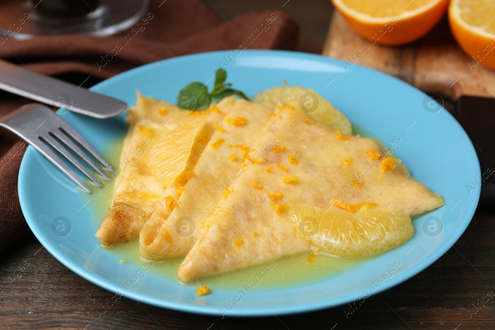 Photo of Plate with tasty crepes Suzette on wooden table, closeup