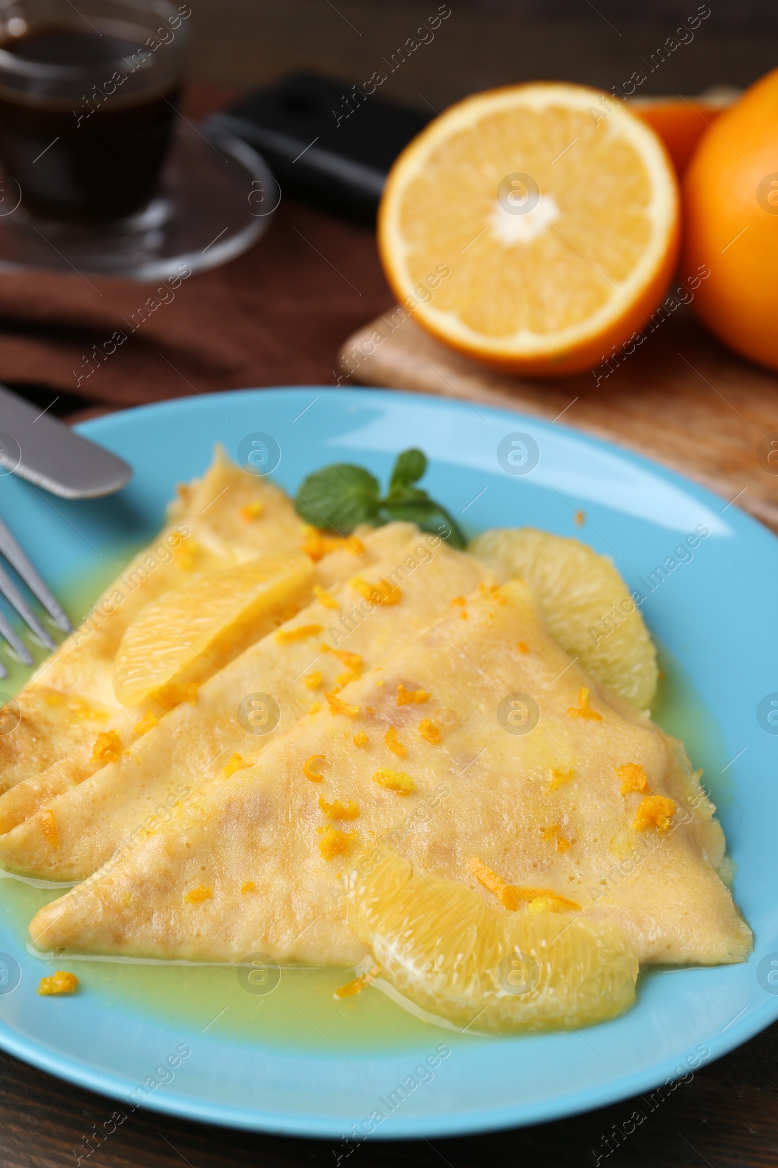 Photo of Plate with tasty crepes Suzette on wooden table, closeup