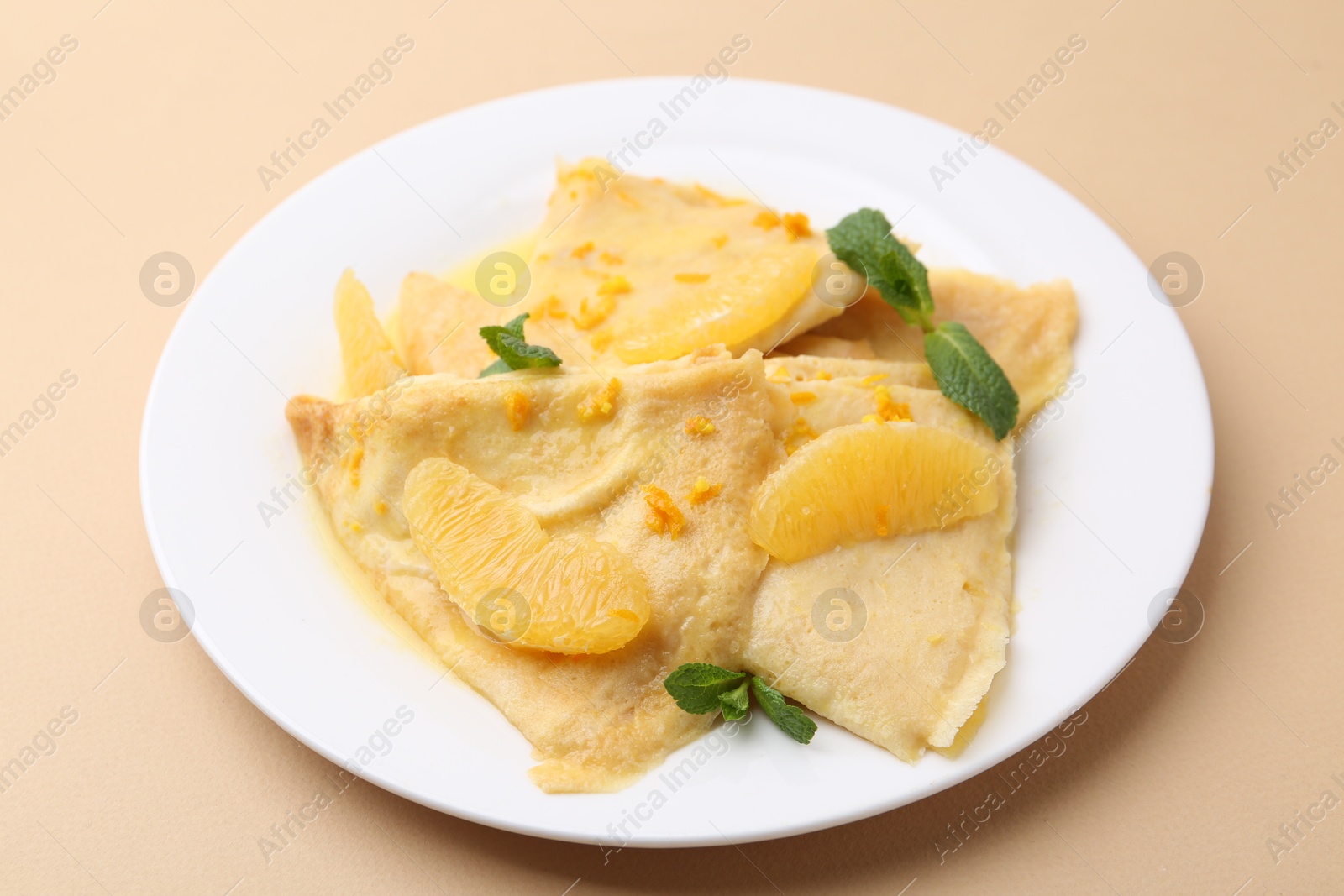 Photo of Plate with tasty crepes Suzette on beige table, closeup