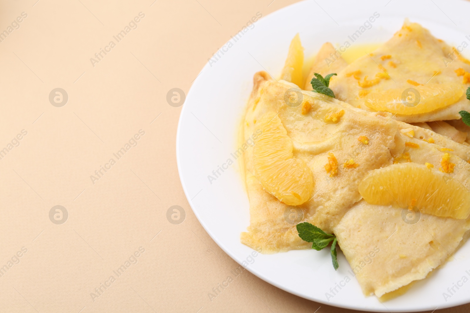 Photo of Plate with tasty crepes Suzette on beige table, closeup. Space for text