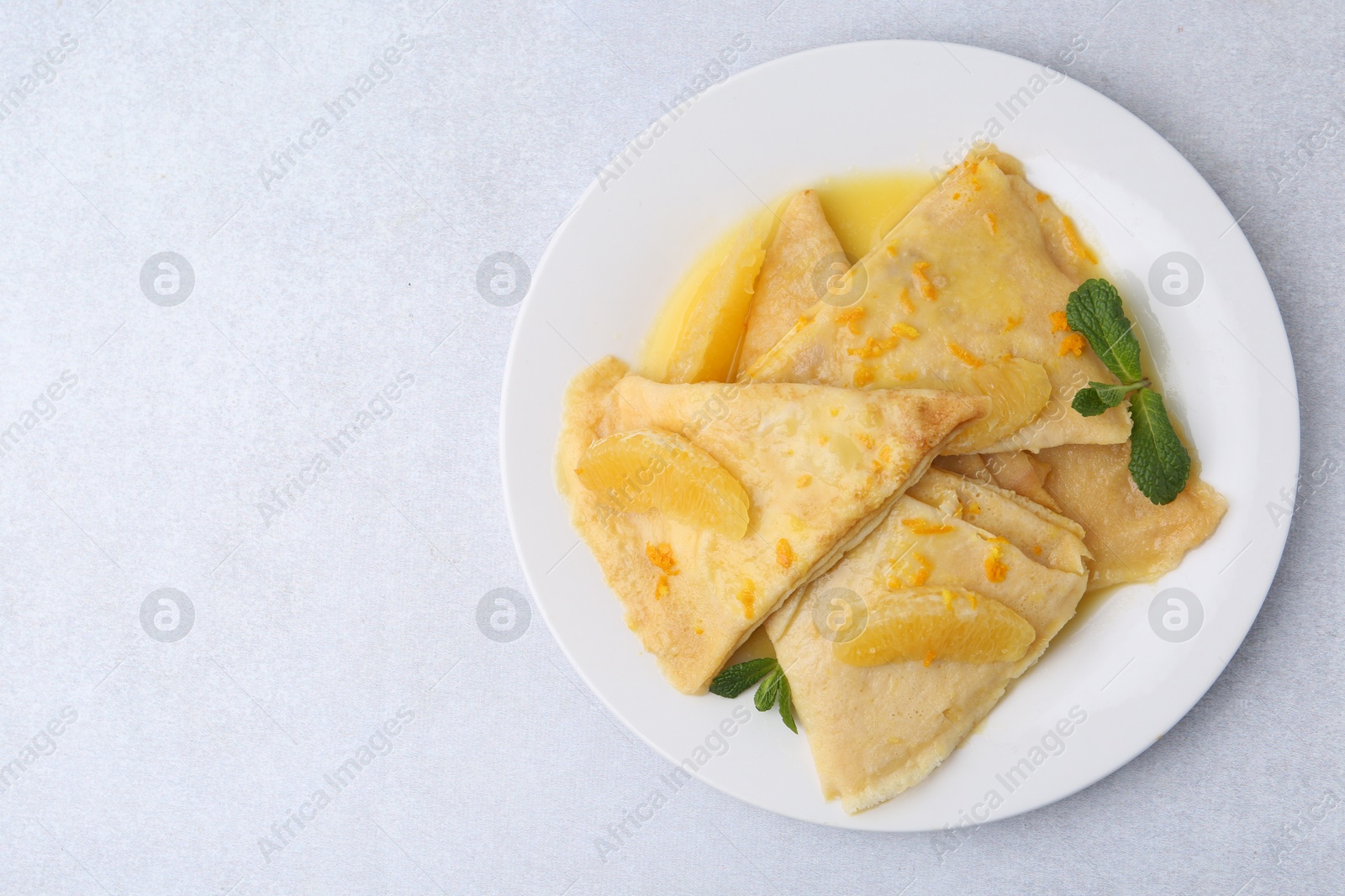 Photo of Plate with tasty crepes Suzette on light textured table, top view. Space for text