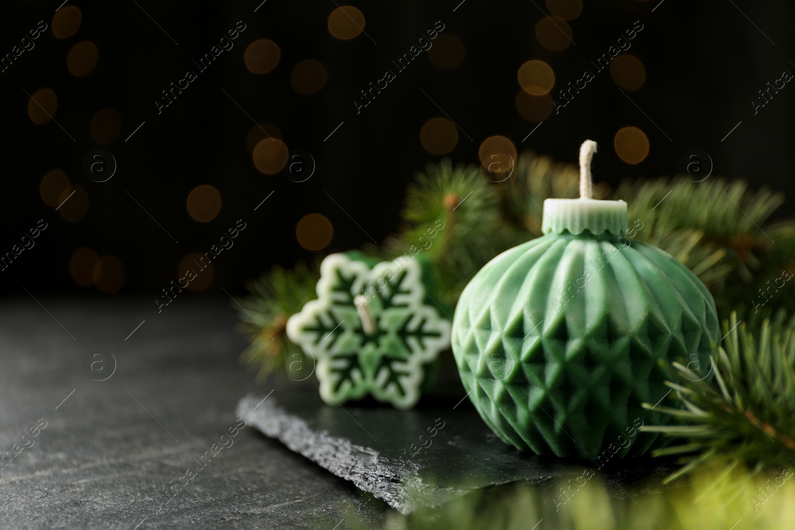 Photo of Soy candles in shape of snowflake and Christmas ball among green fir branches on grey table, closeup. Space for text