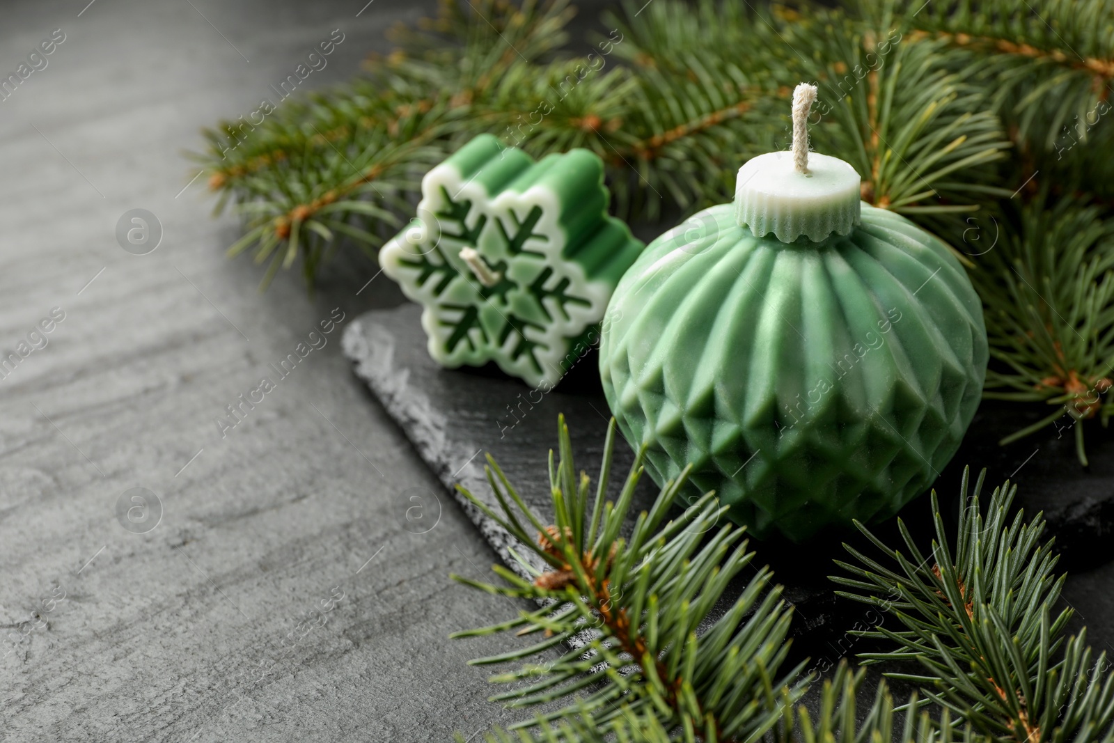 Photo of Soy candles in shape of snowflake and Christmas ball among green fir branches on grey table, closeup. Space for text