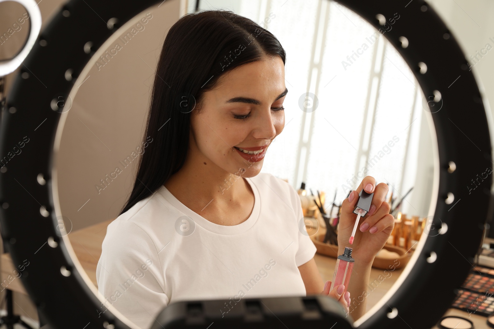 Photo of Beautiful young woman with liquid lipstick indoors, view through ring lamp