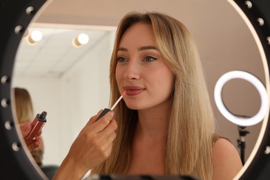 Photo of Professional makeup artist working with beautiful young woman in salon, view through ring lamp