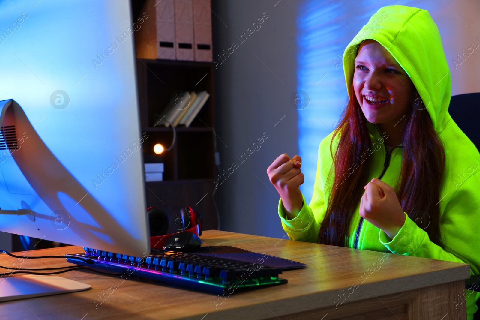 Photo of Happy girl playing video game with keyboard and mouse at table indoors