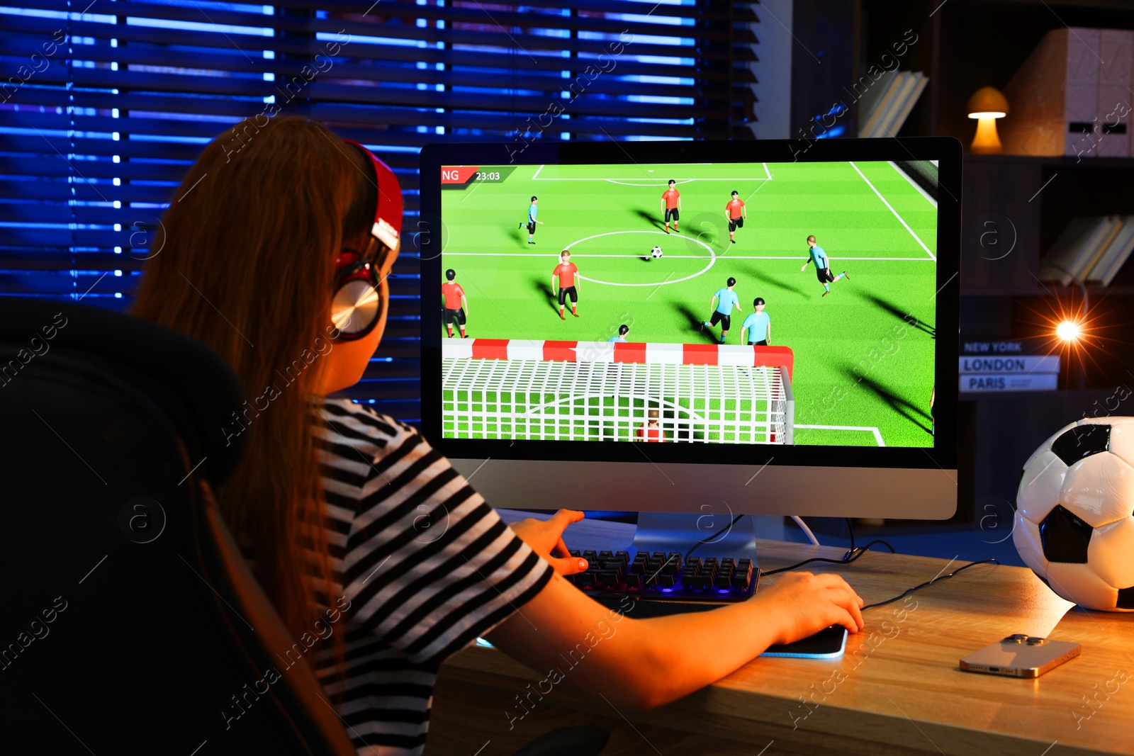 Photo of Girl playing video game with keyboard at table indoors, back view