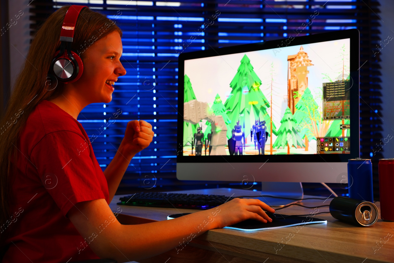 Photo of Happy girl playing video game with keyboard and mouse at table in dark room