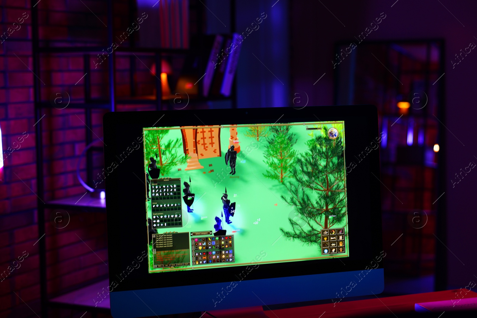 Photo of Computer monitor with videogame on wooden table in dark room