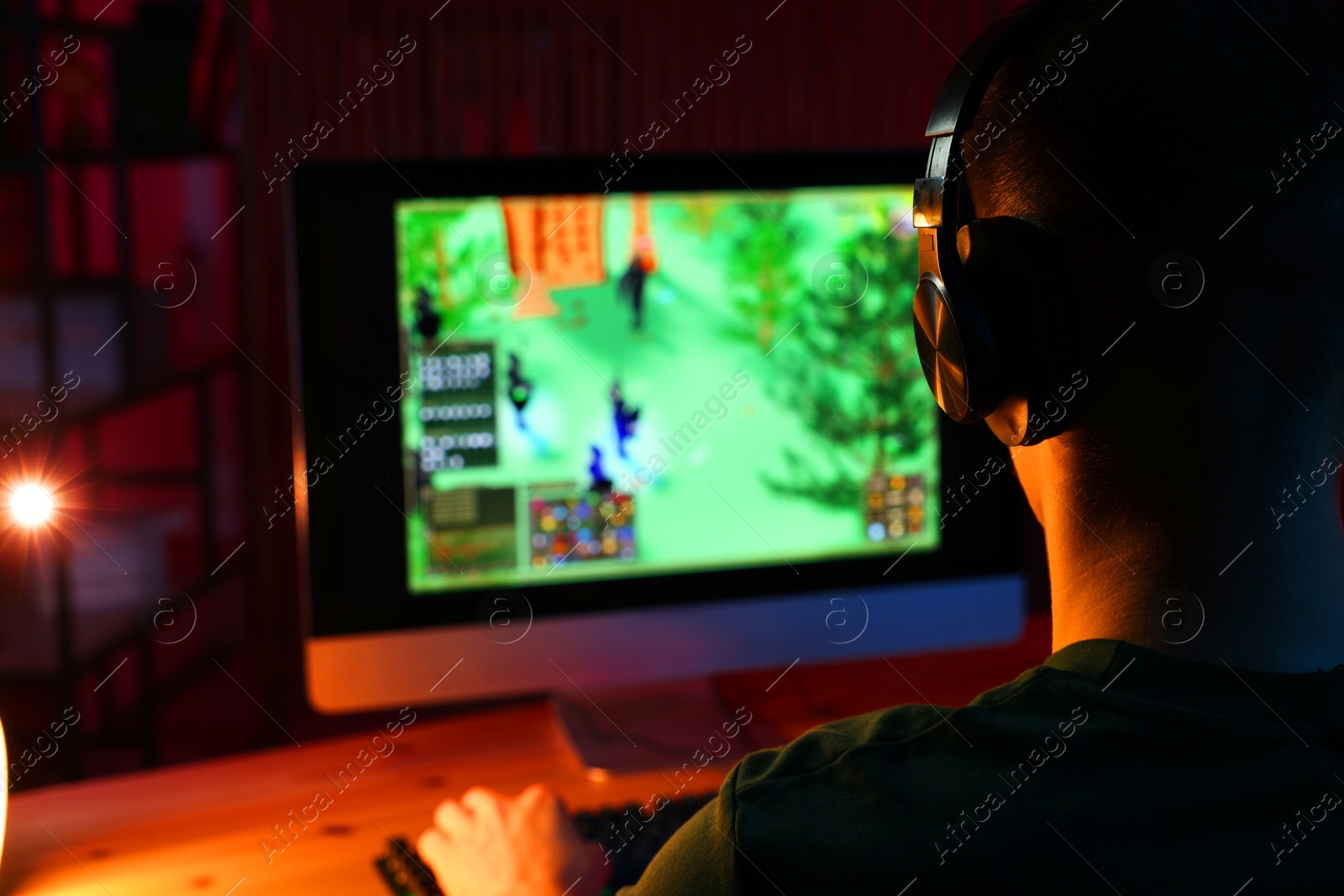 Photo of Young man playing video game with keyboard at wooden table indoors, back view