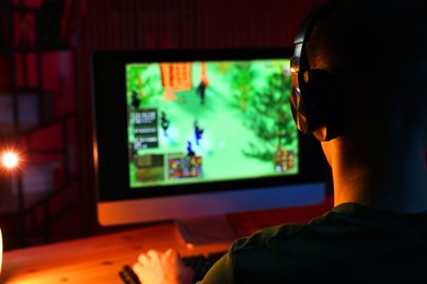 Photo of Young man playing video game with keyboard at wooden table indoors, back view