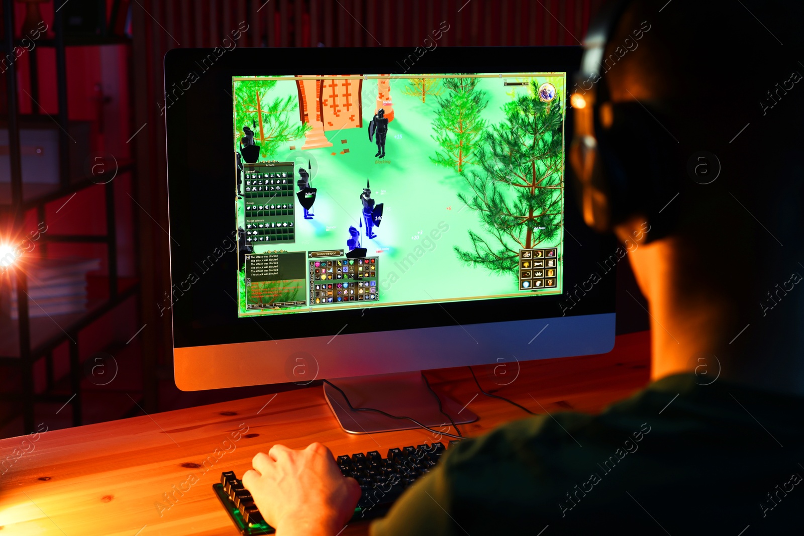 Photo of Young man playing video game with keyboard at wooden table indoors, back view