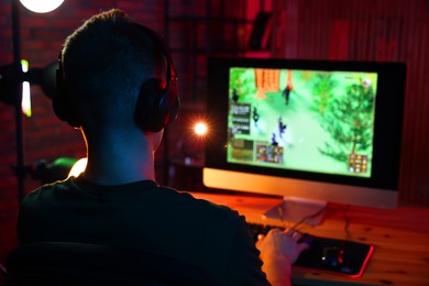 Photo of Young man playing video game with keyboard at wooden table indoors, back view