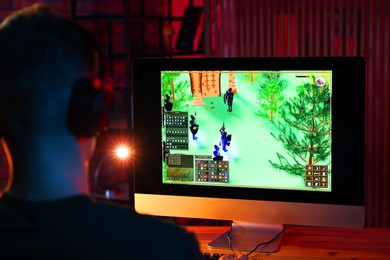 Photo of Young man playing video game at wooden table indoors, back view