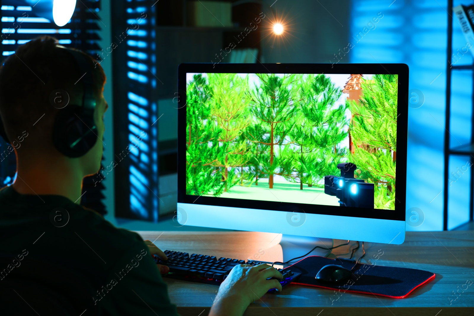 Photo of Young man playing video game with keyboard at wooden table indoors, back view