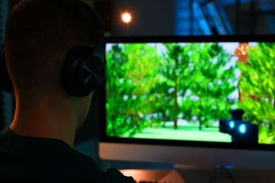 Photo of Young man playing video game at table indoors, back view