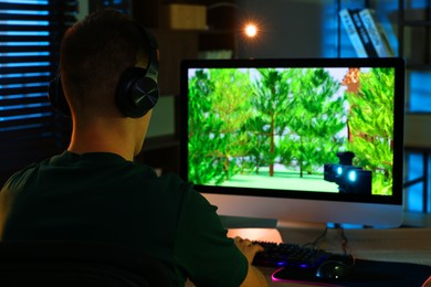 Photo of Young man playing video game at wooden table indoors, back view