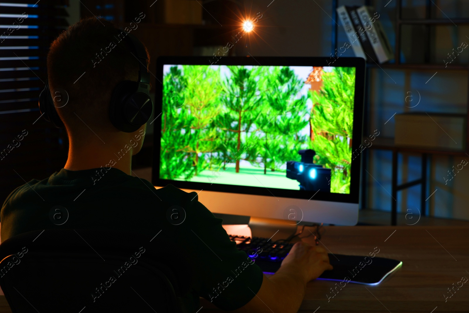 Photo of Young man playing video game with keyboard at wooden table indoors