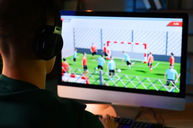 Photo of Young man playing video game at wooden table indoors, back view