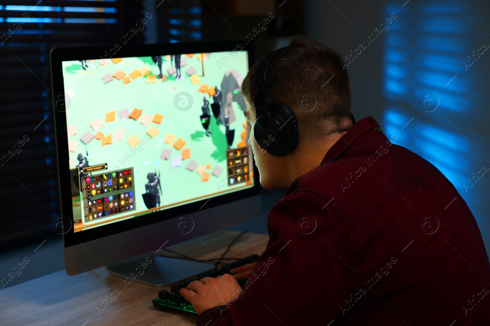 Photo of Young man playing video game with keyboard at wooden table indoors