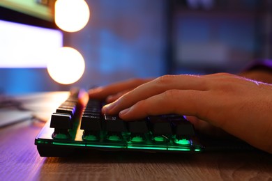 Photo of Young man using computer keyboard at wooden table indoors, closeup