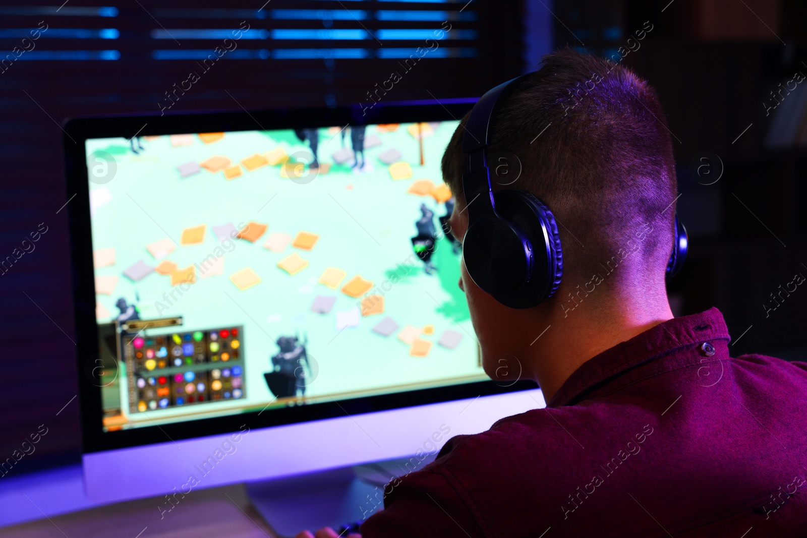 Photo of Young man playing video game at wooden table indoors, back view