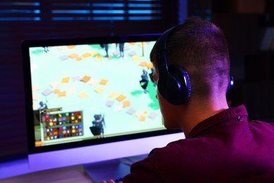 Photo of Young man playing video game at wooden table indoors, back view