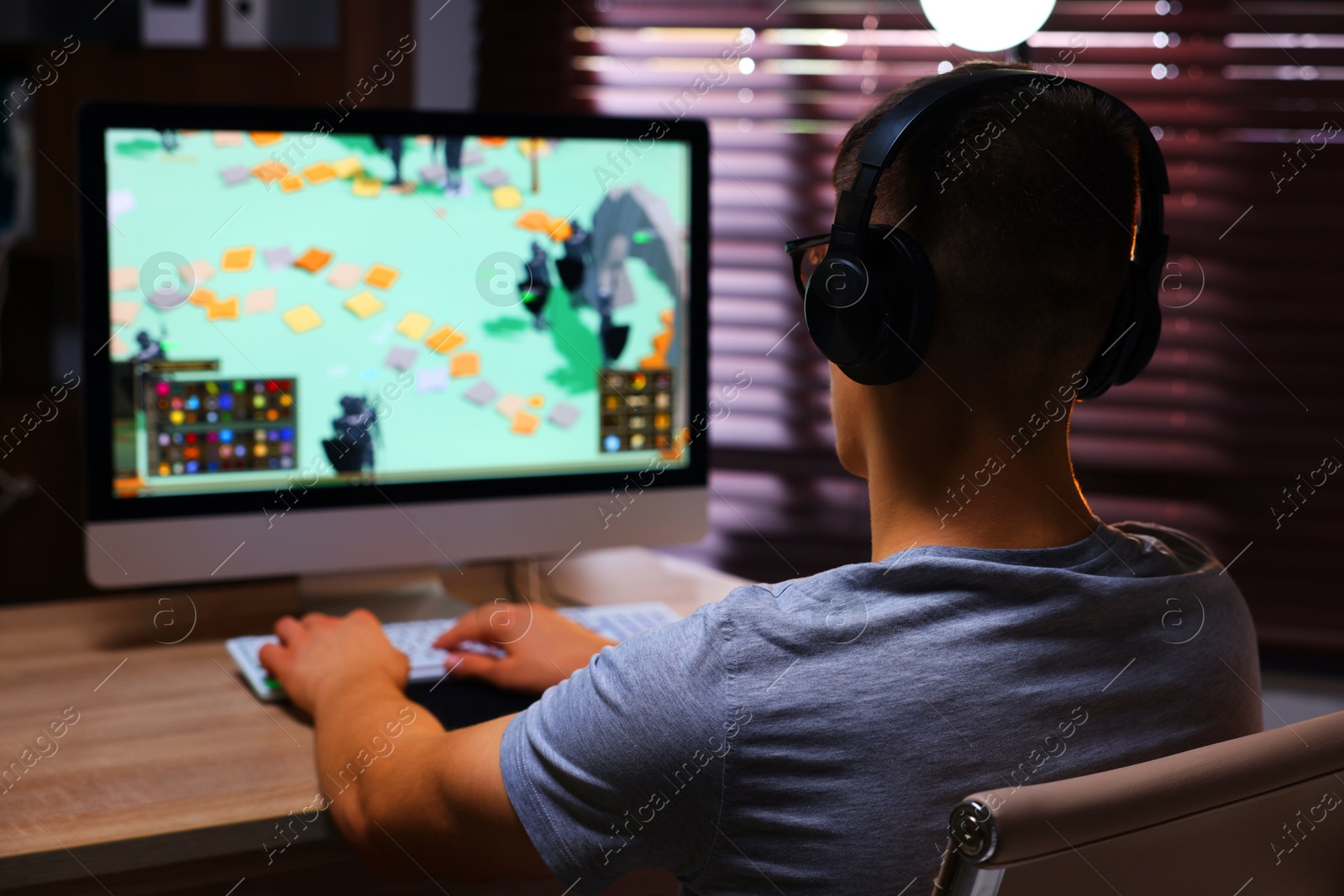 Photo of Young man playing video game with keyboard at wooden table indoors, back view