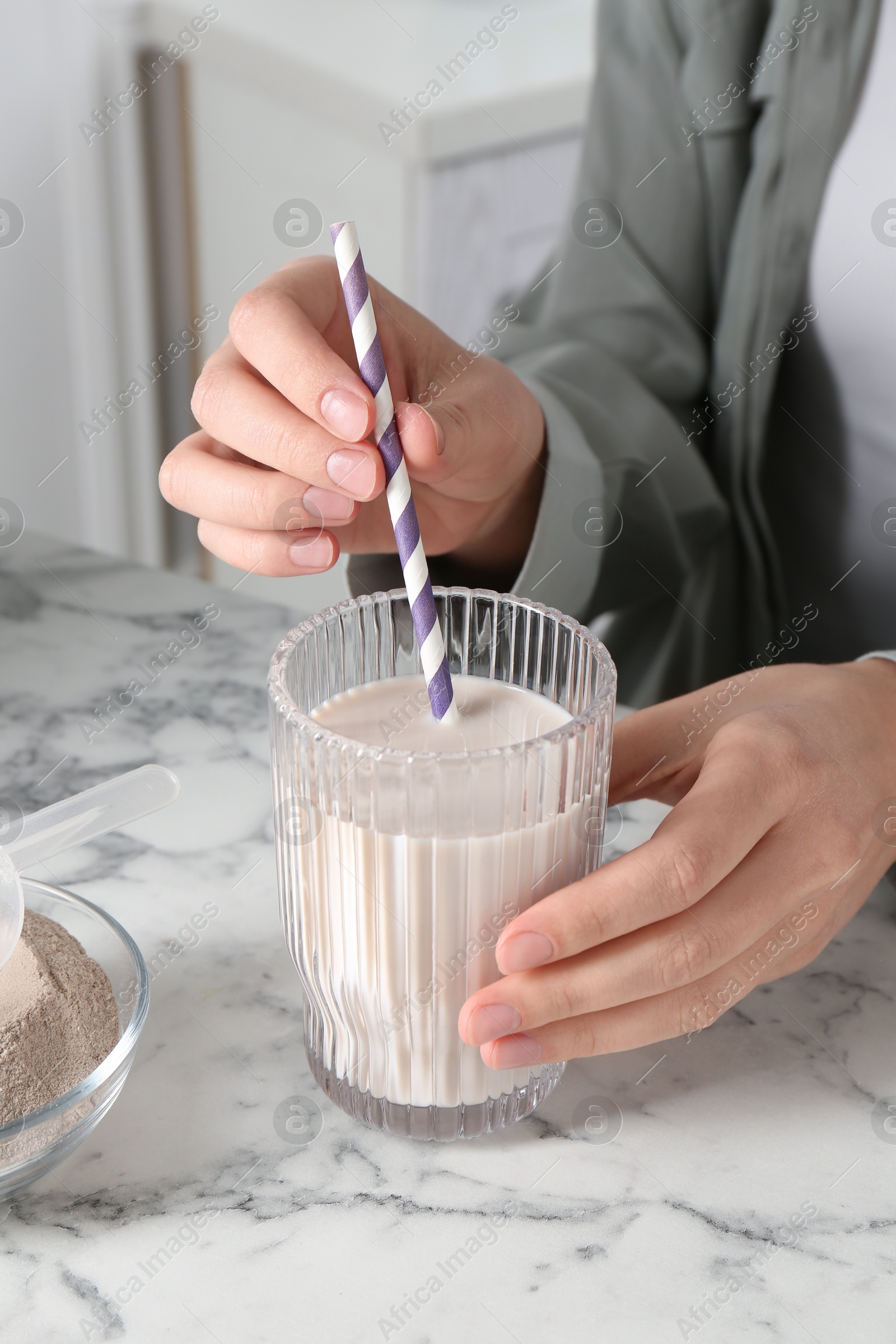 Photo of Woman with glass of protein cocktail at white marble table, closeup