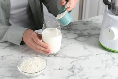 Photo of Making protein cocktail. Woman adding powder into glass with milk at white marble table, closeup