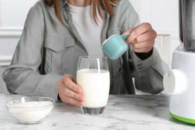 Photo of Making protein cocktail. Woman adding powder into glass with milk at white marble table, closeup