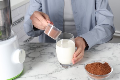 Photo of Making protein cocktail. Woman adding powder into glass with milk at white marble table, closeup