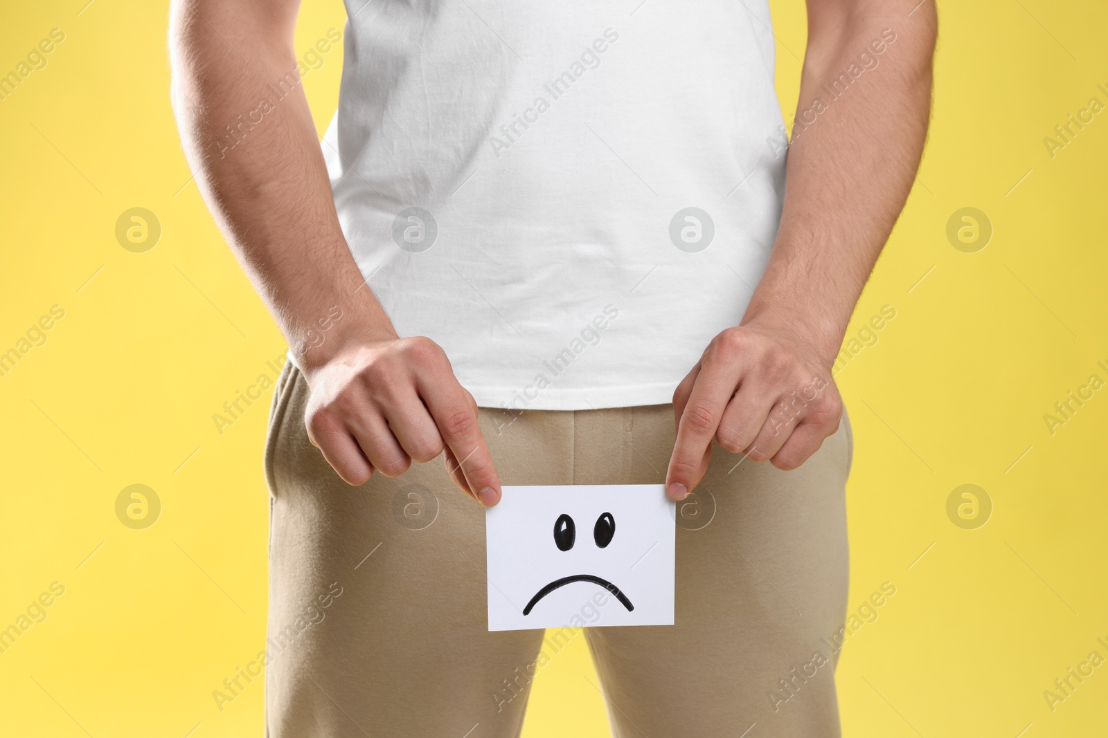 Photo of STD (sexually transmitted diseases). Man holding sticky note with drawn sad face on yellow background, closeup