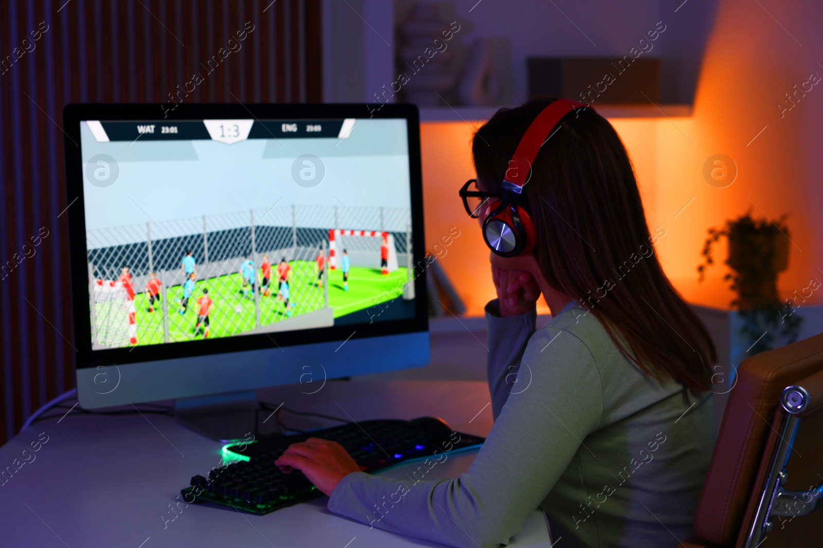 Photo of Woman in headphones playing video game with keyboard at table indoors